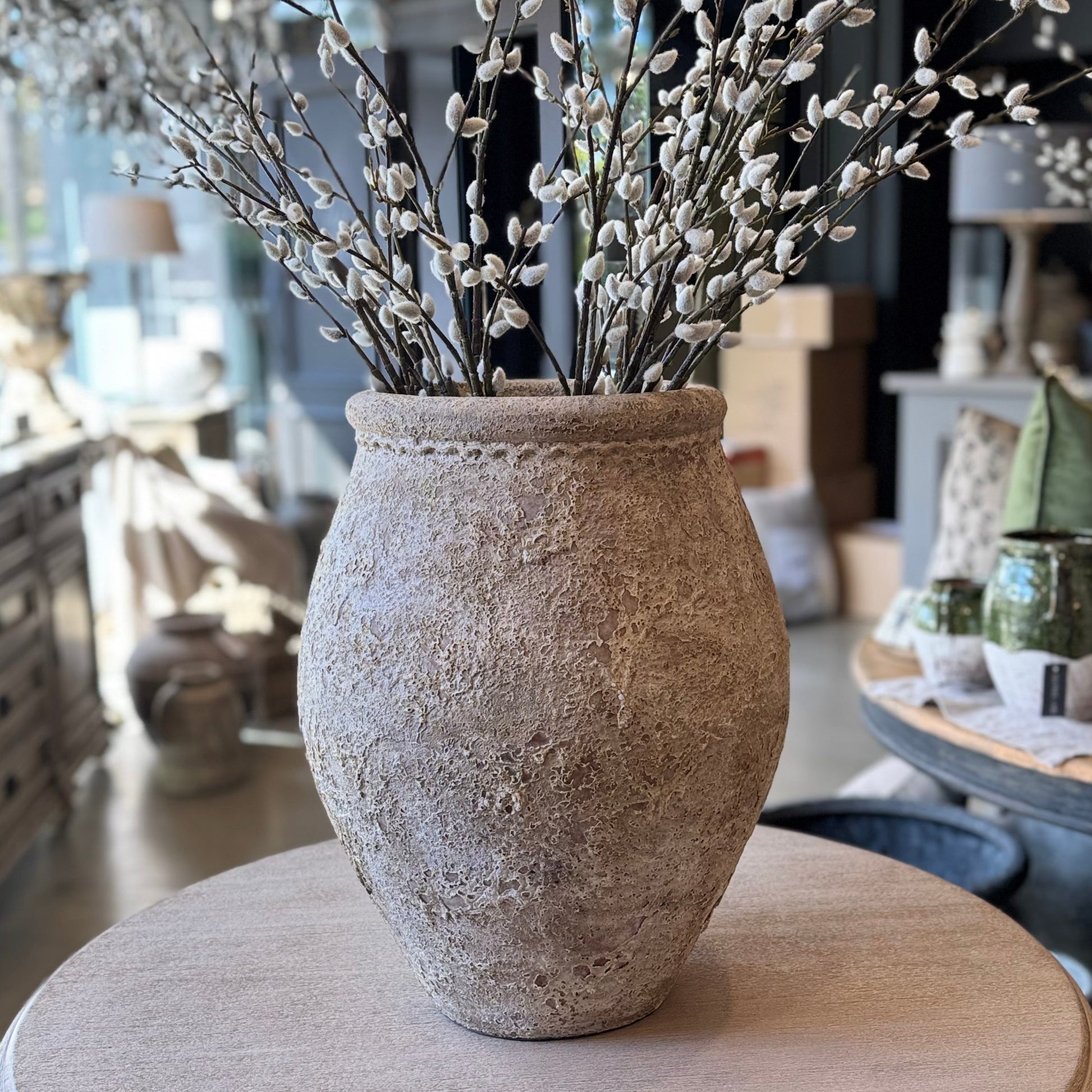 Decorative vase with willow branches on a round wooden table in a home setting.