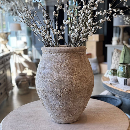 Decorative vase with willow branches on a round wooden table in a home setting.