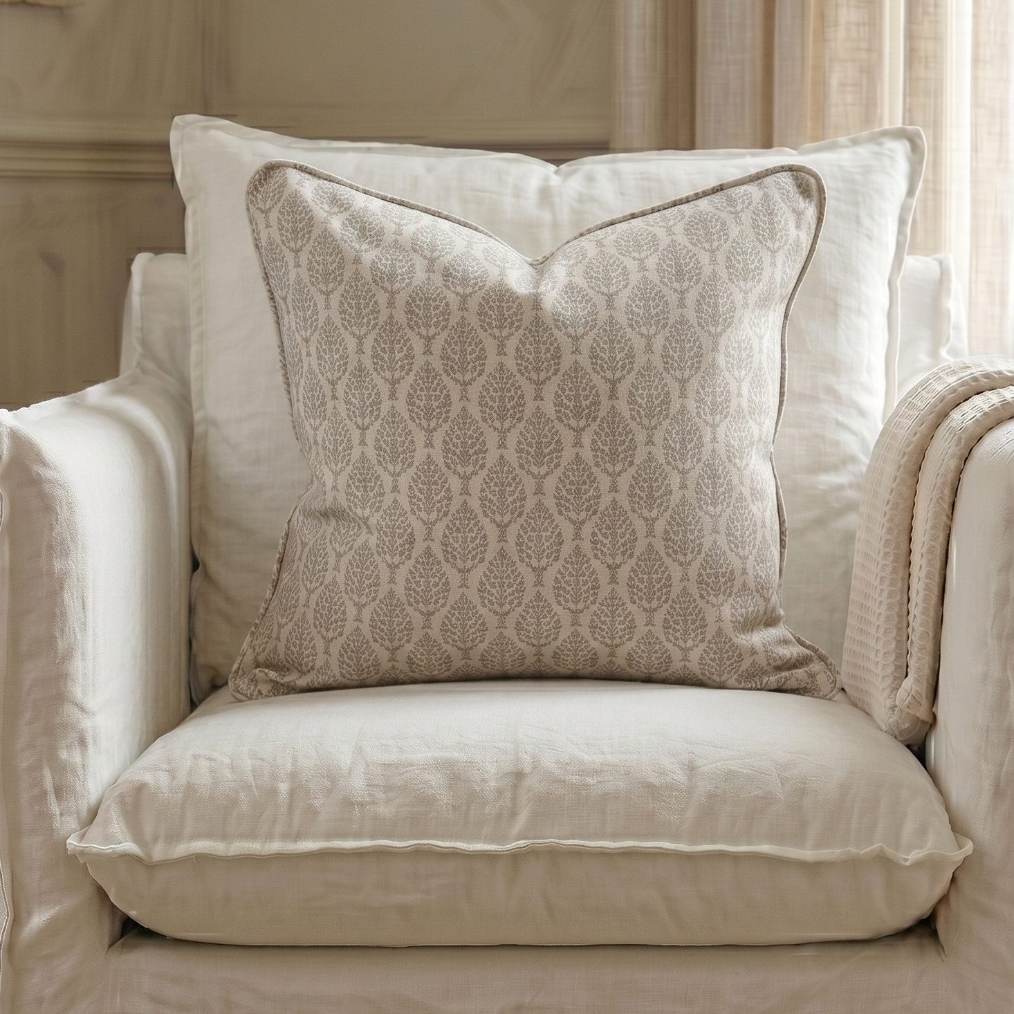 Beige armchair with patterned pillow and blanket in a room with neutral decor.