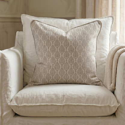 Beige armchair with patterned pillow and blanket in a room with neutral decor.