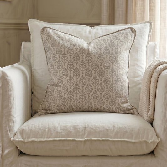 Beige armchair with patterned pillow and blanket in a room with neutral decor.