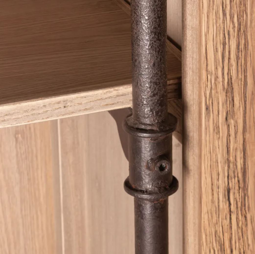 Close-up of a rustic dark metal shelf support pipe or bracket attached to a light oak wood cabinet or shelf frame.