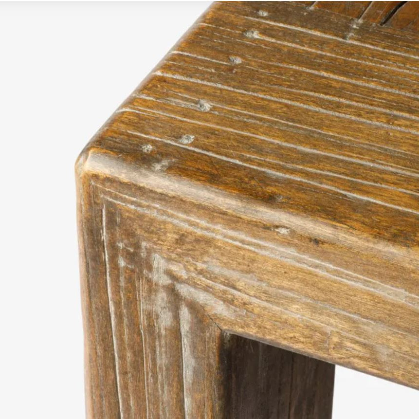 Close-up of the corner of a rustic wooden table with a weathered brown finish and visible grain, against a plain white background.