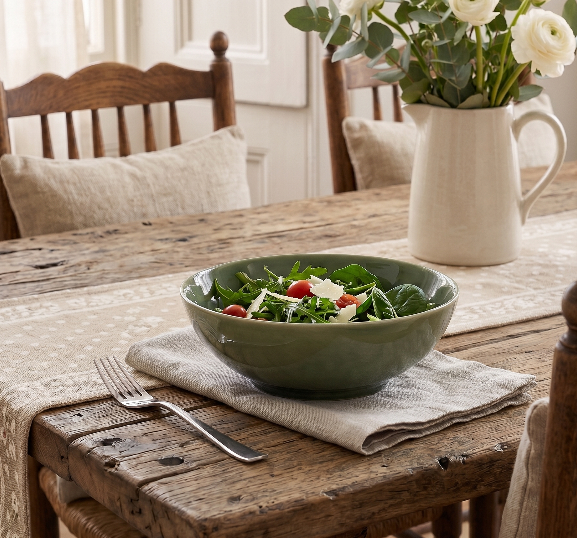 Green salad in a bowl on a wooden table with a vase of flowers.