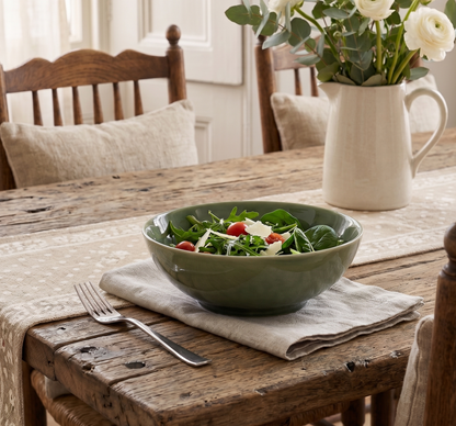 Green salad in a bowl on a wooden table with a vase of flowers.