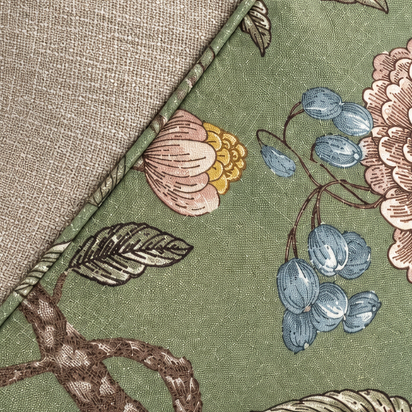 A square decorative throw pillow with a dual-sided design. One side features a textured light beige linen fabric, while the other side has an embroidered floral pattern on an olive green background with pink, blue, and yellow details.