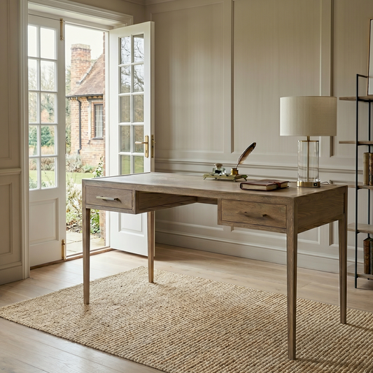 Wooden desk in a home office with a lamp, books, and a feather pen.