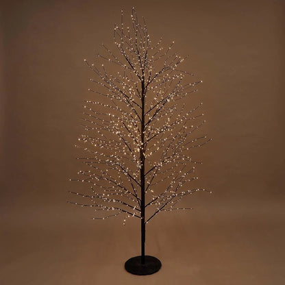 A bare artificial tree with a black trunk and branches, decorated with many small warm white LED lights, standing on a round black base against a plain brown studio background.