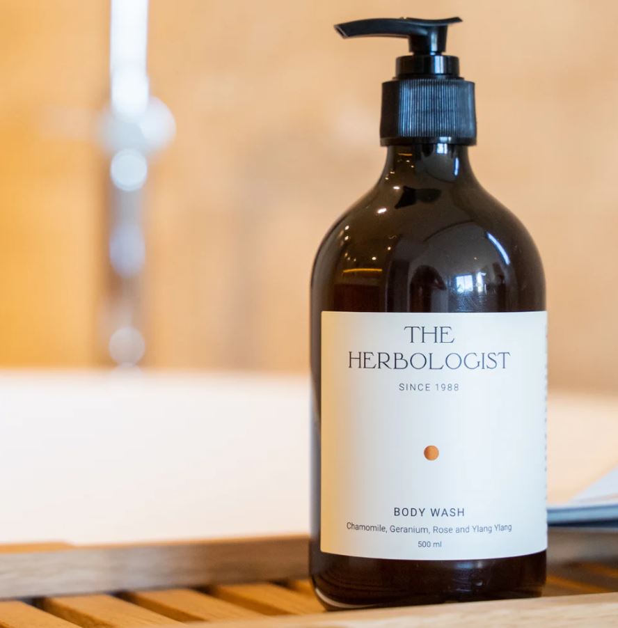 Bottle of 'The Herbologist' body wash on a wooden surface with a blurred background