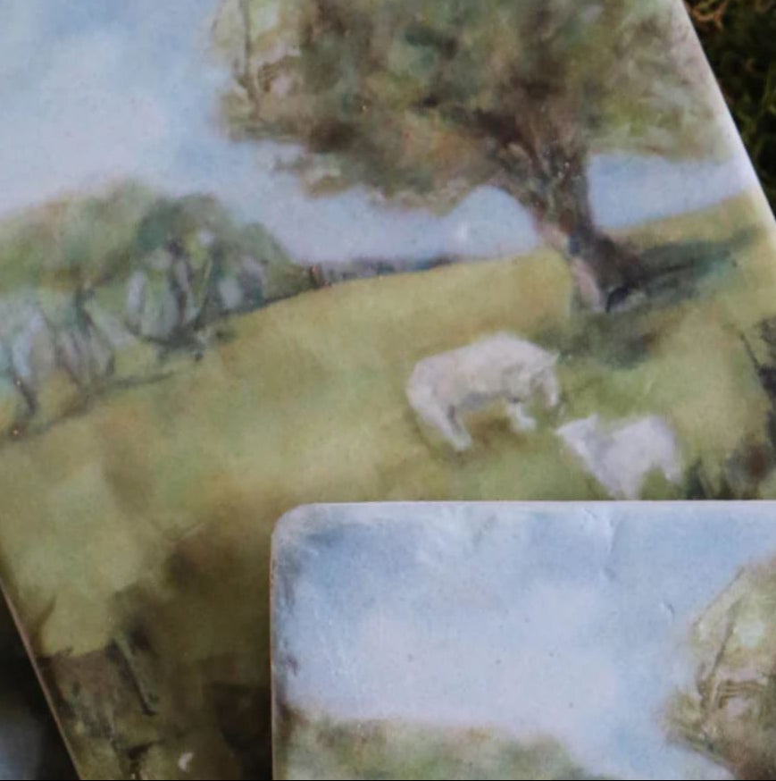 Two ceramic coasters with a scenic landscape design featuring trees and animals.