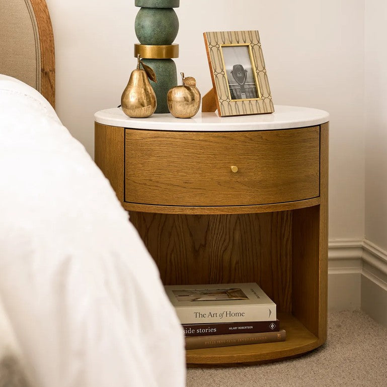 Wooden nightstand with marble top, lamp, and books in a bedroom setting.