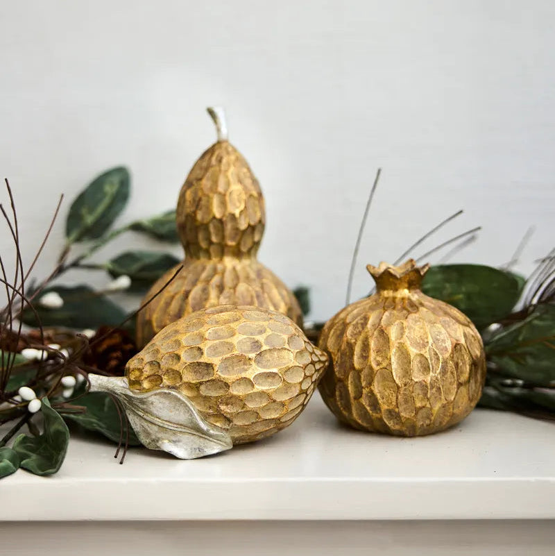 Gold textured gourd-shaped candles on a white surface with greenery