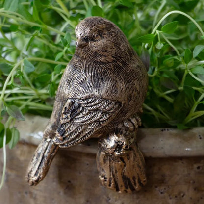 Bronze bird figurine on a stone surface with green plants in the background