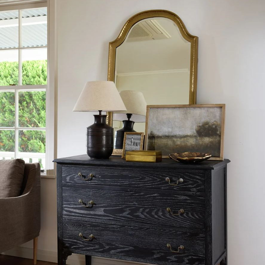 Black dresser with decorative items in a room with a window and chair.