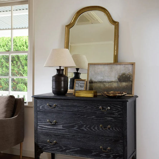 Black dresser with decorative items in a room with a window and chair.