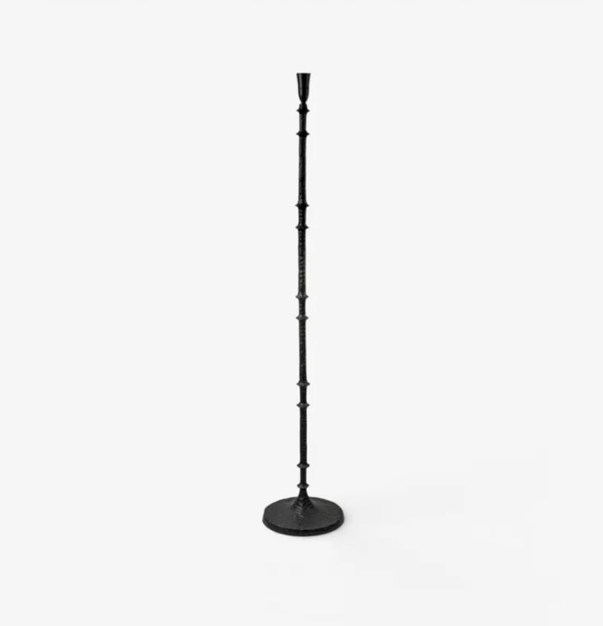 A tall black metal floor lamp with a slender, segmented pole and a round base, shown against a plain white background.