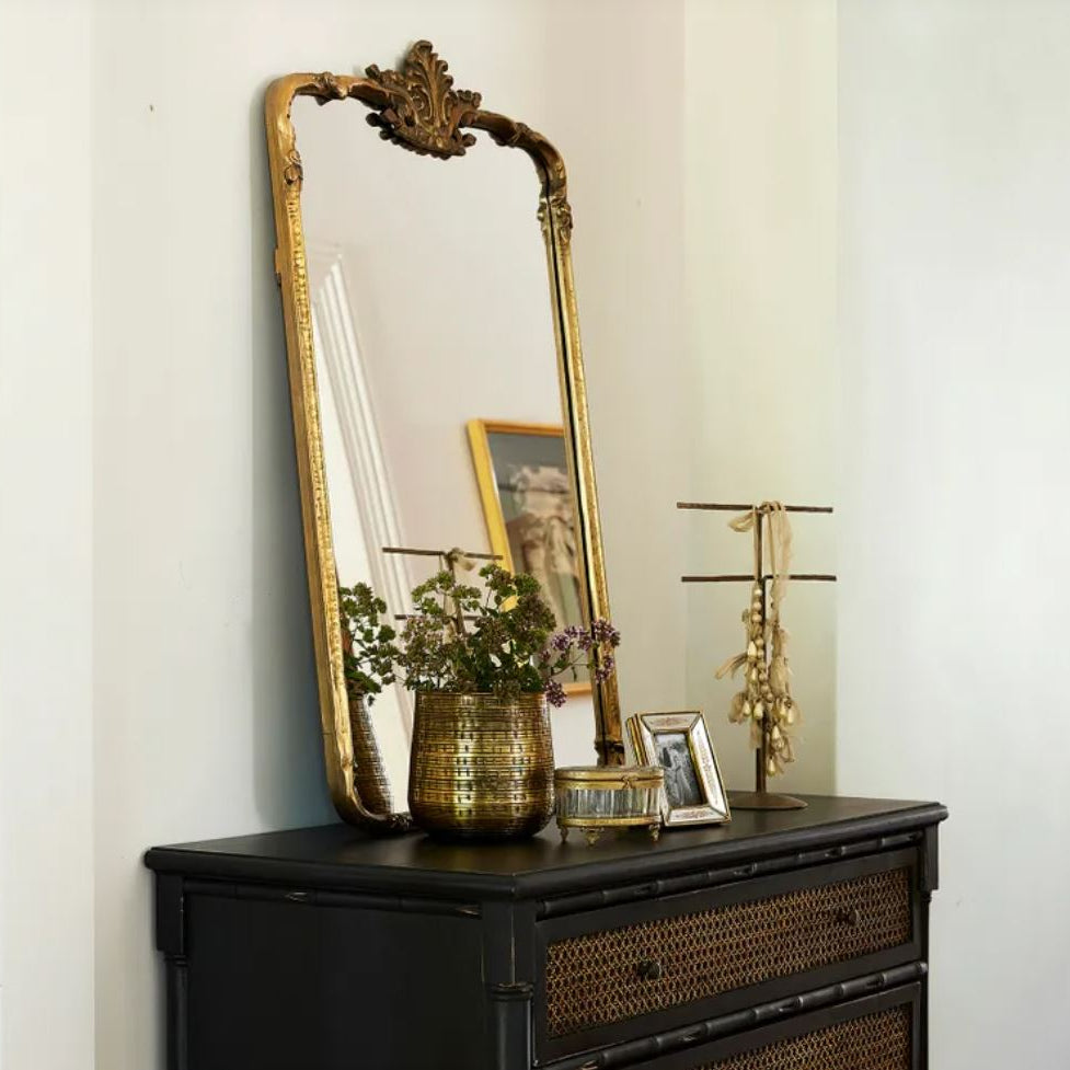 Decorative mirror with gold frame on a black dresser against a white wall