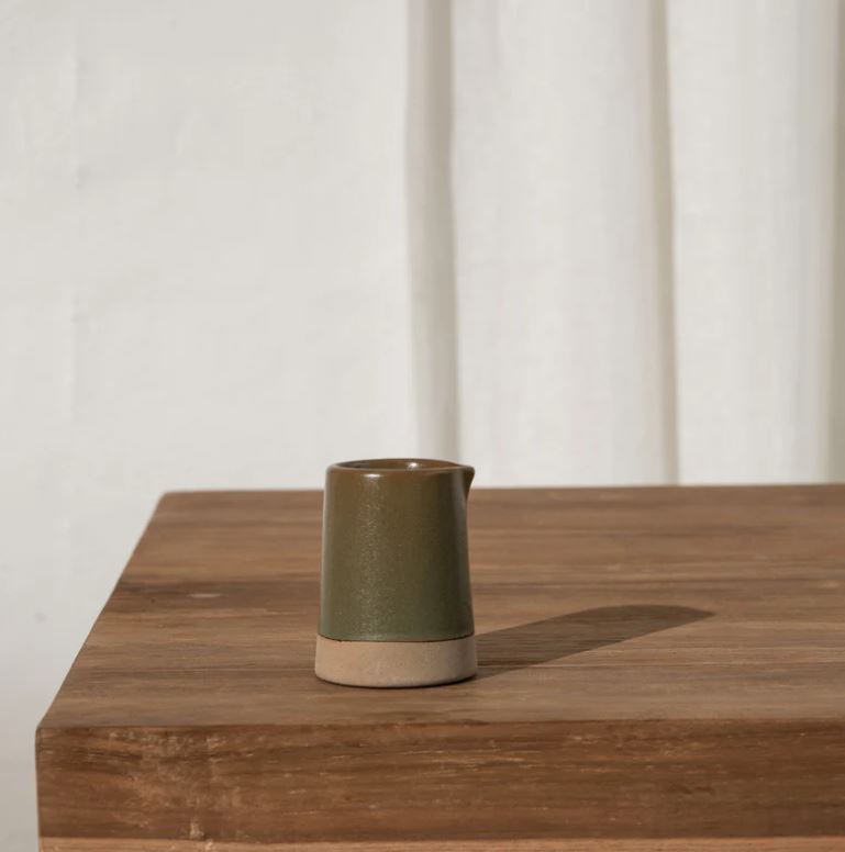Green ceramic pitcher on a wooden surface with a white curtain background