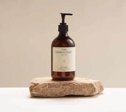 Bottle of 'The Herbologist' body wash on a stone surface with a beige background