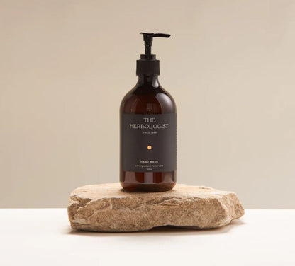 Bottle of 'The Herbolologist' hand wash on a stone surface with a beige background