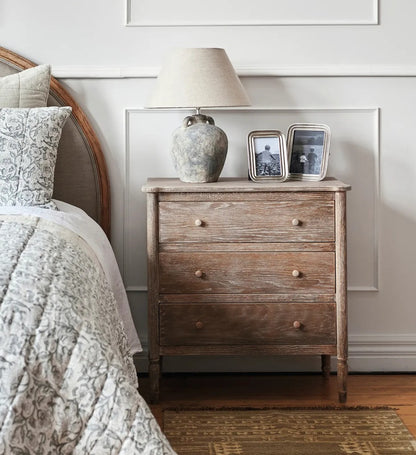 Wooden nightstand with decorative items next to a bed in a bedroom setting