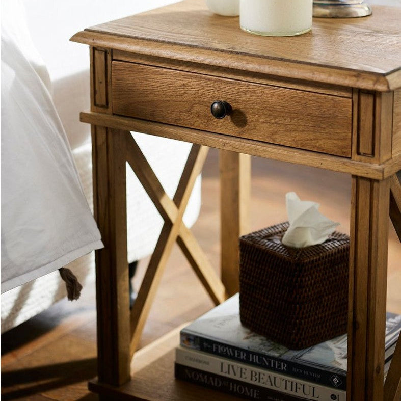 Wooden nightstand with a drawer, books, and a tissue box next to a bed.