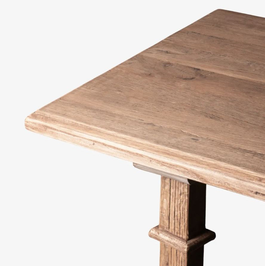 Close-up of a rustic wooden table corner showing the natural wood grain tabletop and a dark wood pedestal leg against a plain white background.
