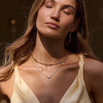Woman wearing layered necklaces and a yellow top against a blurred background