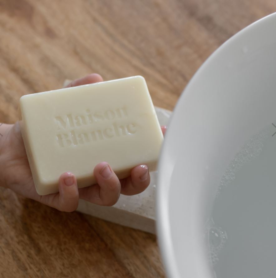 Hand holding a bar of soap labeled 'Blanche' on a wooden surface