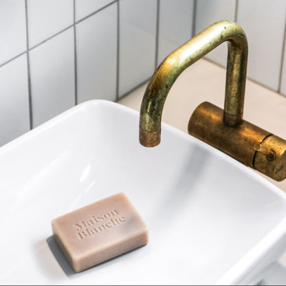 Bar of soap on a white sink with a brass faucet against a tiled wall.