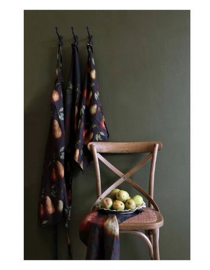 Three patterned cloths hanging on hooks against a green wall with a wooden chair and fruit bowl.