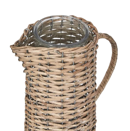 A close-up of a woven wicker pitcher with a clear glass body and handle, shown against a light gray background.