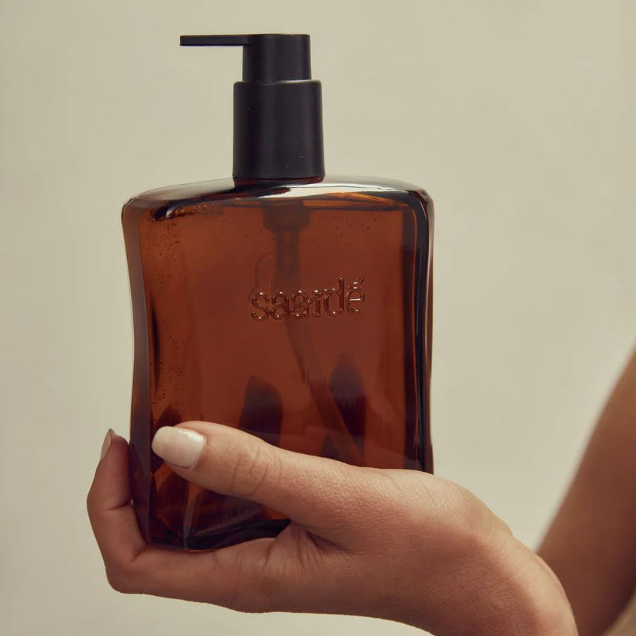 Hand holding a brown bottle with a black pump against a neutral background