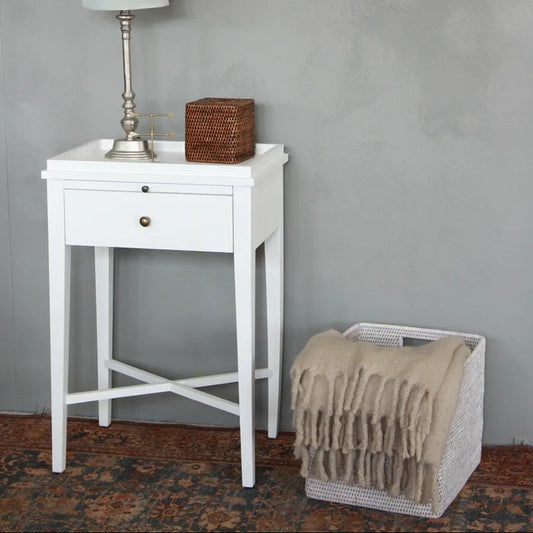 White side table with lamp and basket against a gray wall, next to a wicker basket with a blanket.