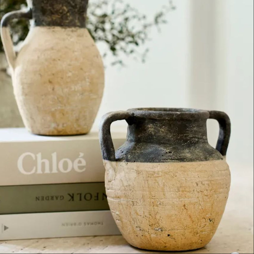 Two rustic ceramic jars on top of books with a blurred natural background