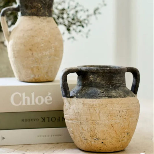 Two rustic ceramic jars on top of books with a blurred natural background