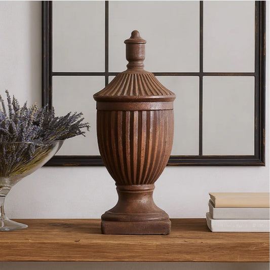 Decorative brown urn on a wooden surface with a mirror and books in the background
