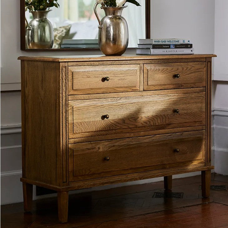 Wooden dresser with decorative items including a vase and books, against a neutral wall.