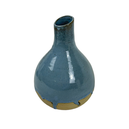 Indulge in the exquisite craftsmanship of Indonesian artisans with the Okta Handcarved Blue Ceramic Vase. Its stunning sky blue glaze beautifully complements the raw, unglazed base for a truly captivating piece. Front.